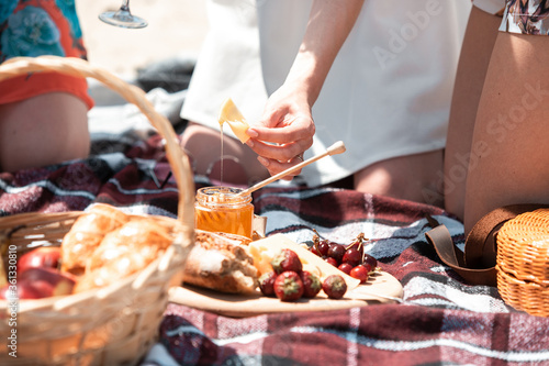 Picnic bread, croissant basket with fruit on cloth with bright sunlight. Croissant, honey, strawberry. Healthy choice for spending time on nature in summer day. Food, nutrition, healthy eating.