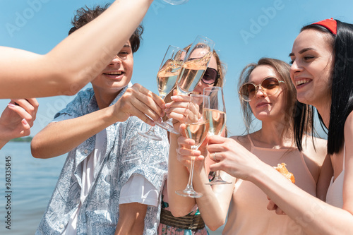 Close up clinking, cheers. Seasonal feast at beach resort. Group of friends celebrating, resting, having fun in sunny summer day. Look happy and cheerful. Festive time, wellness, holiday, party.