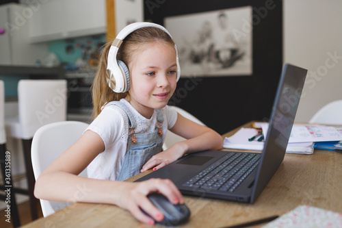 beautiful young girl with headphones and laptop is doing homeschooling during corona covid 19
