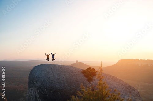 Two friends have fun and jump on top of the mountain