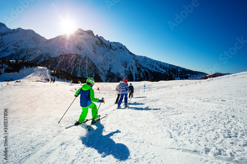 Group of children ski on the hill together on Alpine resort over mountains on background