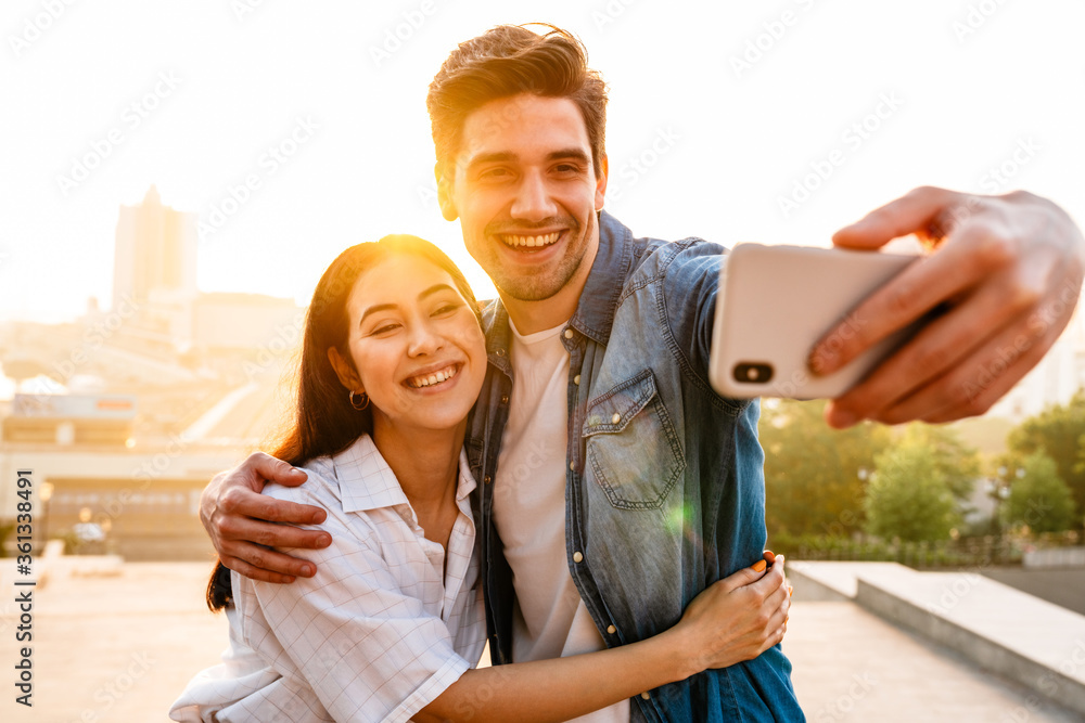 Image of smiling couple hugging and taking selfie photo on cellphone