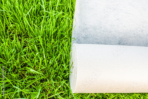 A roll of white geotextile lies on the green grass outside photo