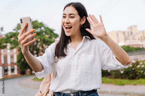 Photo of happy asian woman using cellphone and waving hand © Drobot Dean