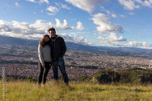  A couple standing and looking ahead on a hill, under a sky with sparse clouds and sunny, with a huge city in the background © john