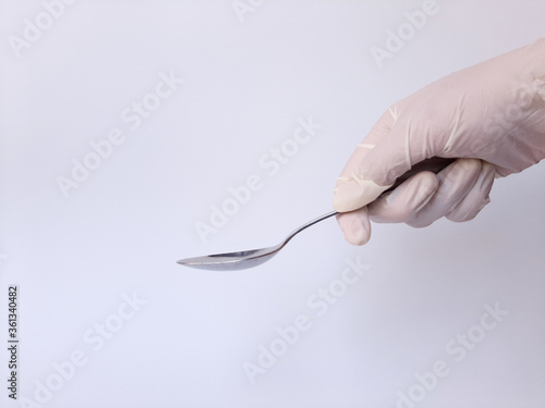 A hand with white latex glove holds metal spoon. Isolated on a white background