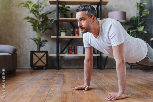 Concentrated middle adult man doing push ups exercise at home