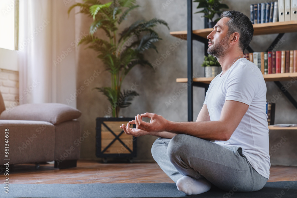 Meditation concept. Calm man meditating while sitting in lotus position relaxing doing yoga at home - obrazy, fototapety, plakaty 