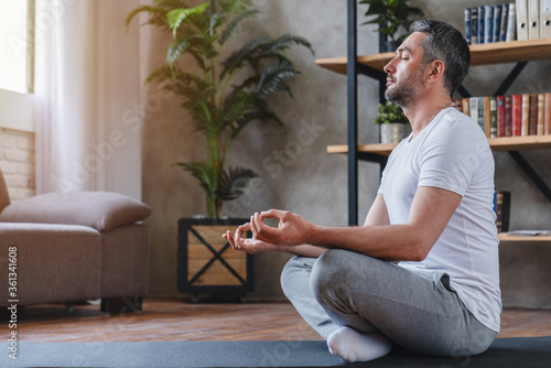 Meditation concept. Calm man meditating while sitting in lotus position relaxing doing yoga at home