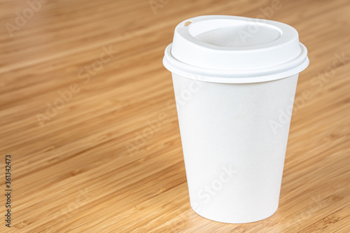 Mockup a disposable paper cup of coffee to go on wooden table.