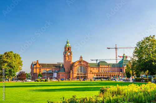 Wiesbaden Hauptbahnhof central railway station Neo-baroque style building and Reisinger-Anlagen park with green trees and lawn in historical city centre, blue sky background, State of Hesse, Germany