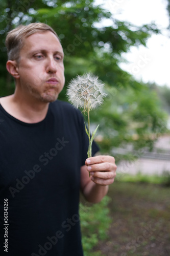 A man with puffed up cheeks is blowing on a blowball. 