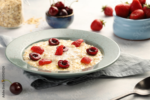 Oatmeal with milk and butter, with strawberries, and ripe cherries. A delicious and healthy breakfast, rich in vitamins and minerals.