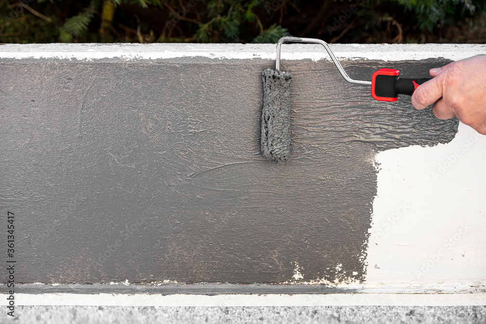 painting a concrete wall with a paint roller and grey paint Stock Photo