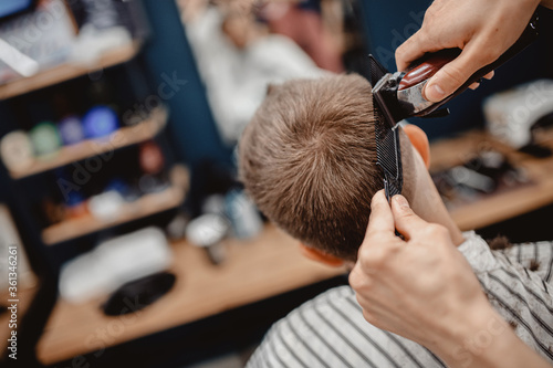 Barber in Barbershop shear hair electric to young guy for fashionable hairstyle