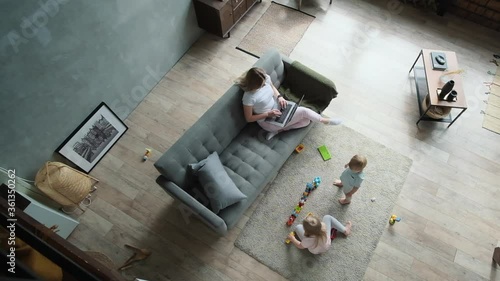Young mother working at home and cute blond kids playing cozy apartment top view