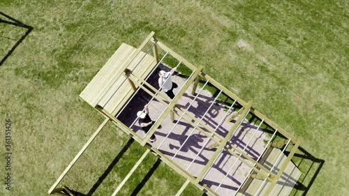 Aerial from above of two young white Caucasian men in pike shirts competing in an obstacle course made of eco friendly wood materials at a vacation travel resort in Sweden with green grass swinging photo