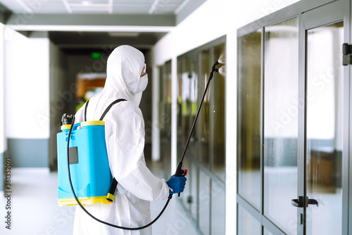 Contractor disinfecting office for COVID-19 coronavirus. A disinfector man in a protective suit and mask sprays disinfectants in office. Prevention of spreading pneumonia virus with surfaces.