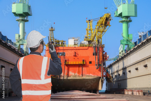 Workers speaking radio walkie talkie in hand holding on dry dock, large cargo ship maintenance and repair