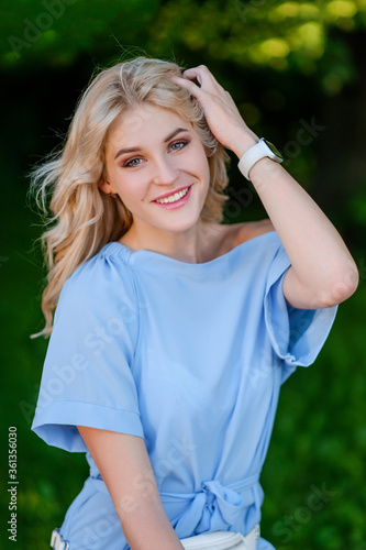 Portrait of a young beautiful girl 21 years old in a blue summer dress with a white belt bag. The woman smiles. Beautiful lips and eyes. Long loose hair.