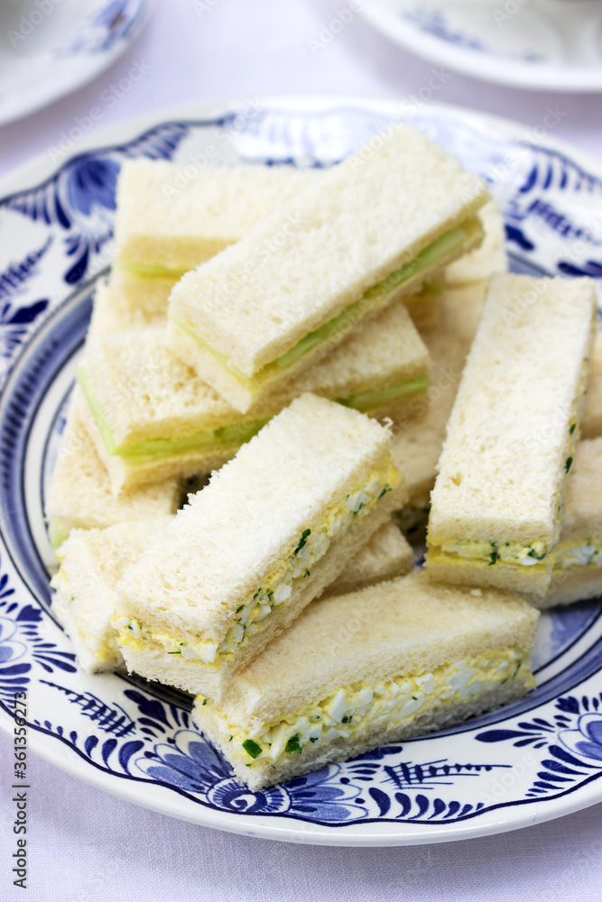 Afternoon tea in the garden, finger sandwiches with cucumber and egg salad and tea on a light background.