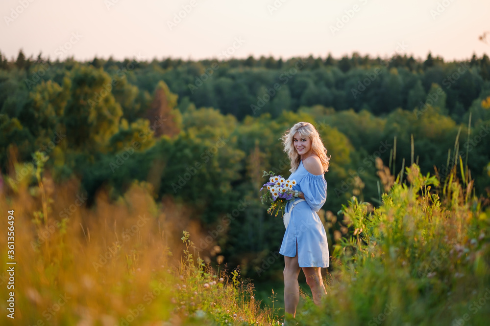 Portrait of a young beautiful blonde girl in a blue dress. Loose hair, sensual lips and big blue eyes. A woman holds a bouquet of daisies wildflowers .