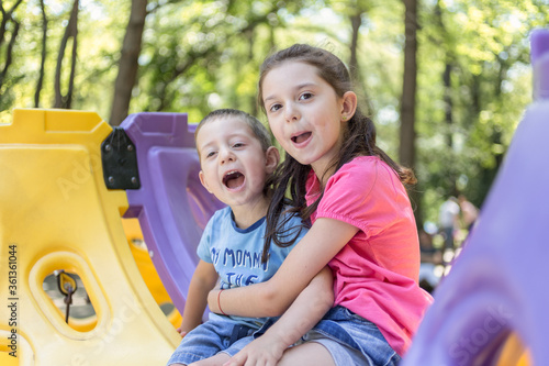 A portrait of smiling little girl and a boy enjoys playing in a children playground. Having fun outdoor.