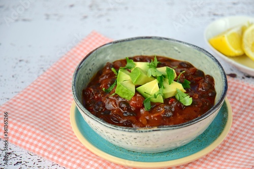 Homemade vegan black bean chili tomato soup with diced avocado and chopped parsley served with lemon