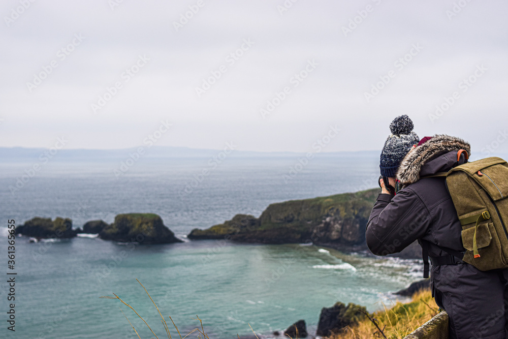 Photo of a young and attractive man with beard standing in the nature with winter clothes and a backpack in the Giants Causeway, Belfast. Holidays concept