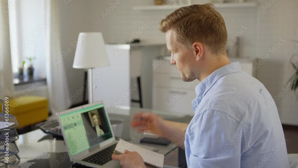 Businessman taking notes in notepad while having video call with business partner on laptop computer. Man finishing online meeting, closing pc, reviewing notes and thinking sitting at table at home Businessman taking notes in notepad while having video call with business partner on laptop computer. Man finishing online meeting, closing pc, reviewing notes and thinking sitting at table at home