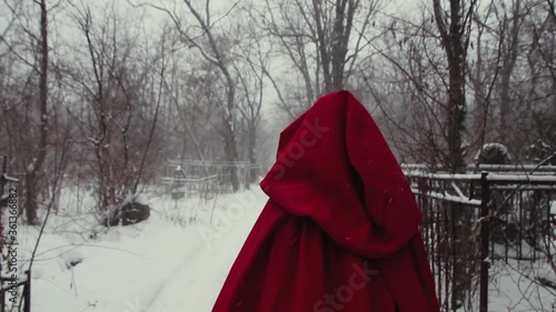 Little Red Riding Hood. A girl in a red coat with a hood walks through a snowy cemetery in winter. Snowing in slow motion