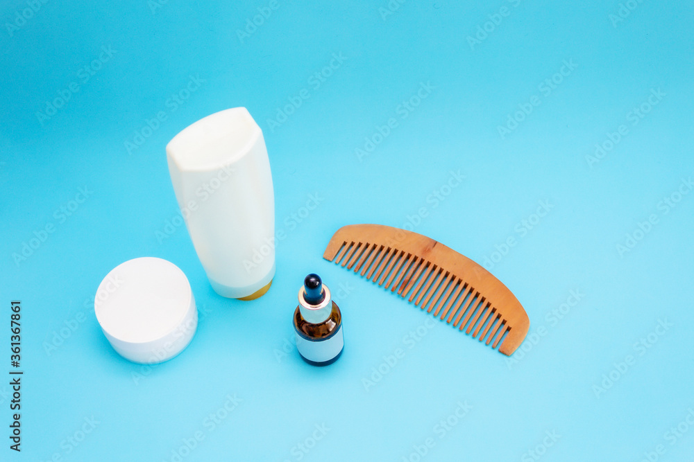 Obraz premium white round cream jar, pipette jar, wooden comb, large white bottle are on a blue sky background, front view