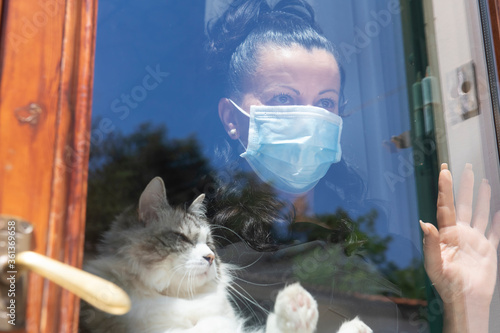 Woman holding a cat behind a window wearing a Covid-19 protective face mask