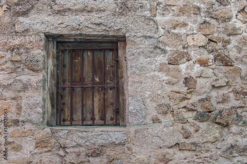 stone wall with closed wooden window and metal fence