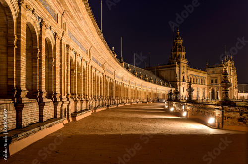 Balcony at Night - A close-up night view of the illuminated second-floor balcony of the semi-circular brick building at Plaza de España, Seville. Andalusia, Spain.