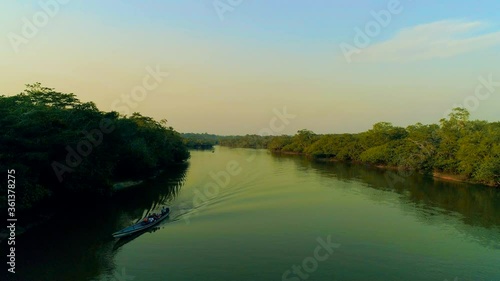 Aerial Shot Of Boat With Tourists Quickly Leaving Tiny Waves Behind On Beautiful Amazon Turquoise River Reflecting Amazing Sunset Between Dense Rainforest In Cuyabeno National Park