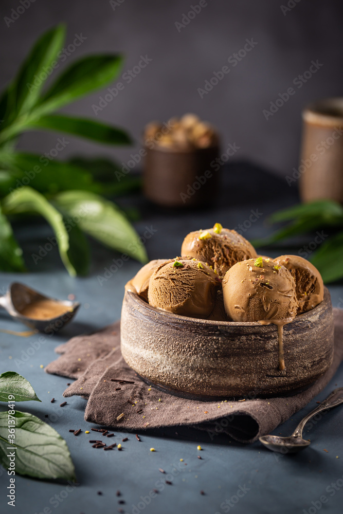 Scoops of coffee or chocolate ice cream in a bowl with green leaves on dark background