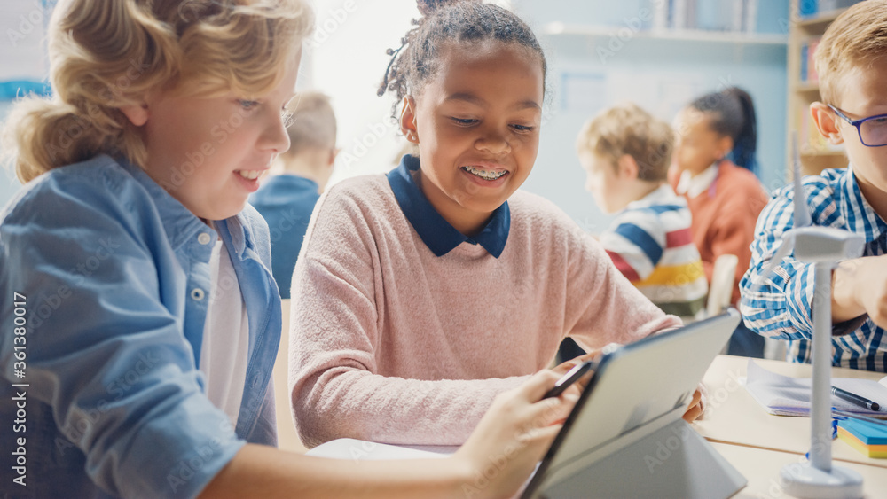 Fototapeta premium In the Elementary School: Girl and a Boy Work as a Team Using Tablet Computer. Diverse Classroom with Kids Learning Programming Language and Software Design