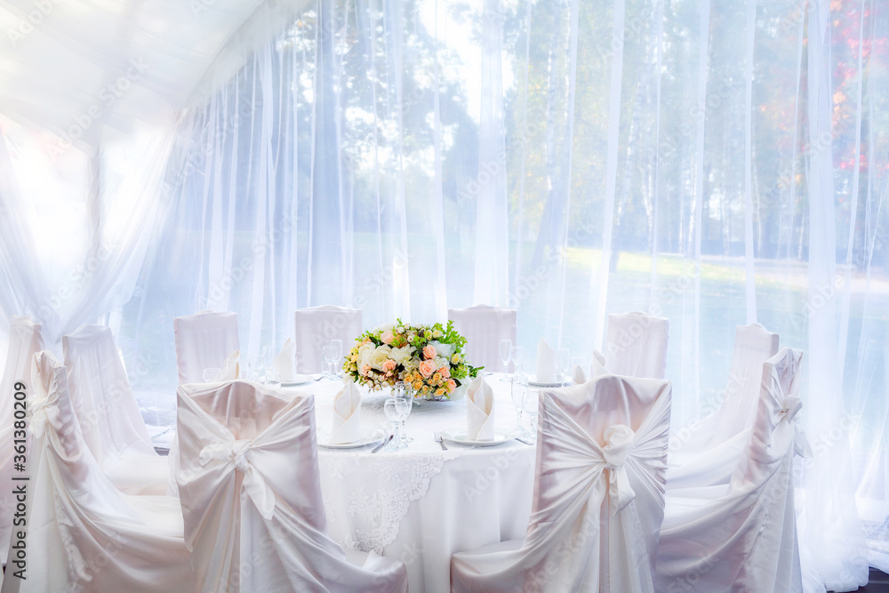Wedding table with a white tablecloth in a white outdoor tent