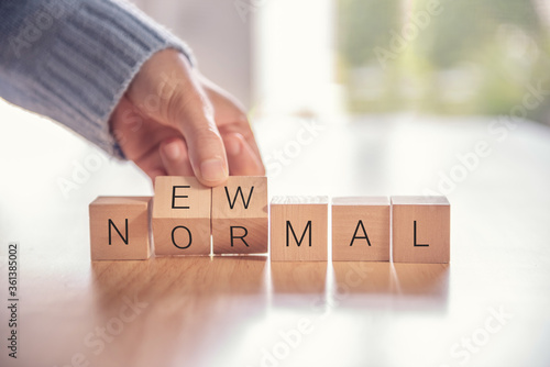 Woman hand arranging wooden cubes with NEW NORMAL word. Adapting to new life or business post-lockdown after coronavirus pandemic. Business with social distancing personal hygiene.