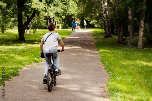 A teenager rides a Bicycle in the Park. Cyclist view from the back.