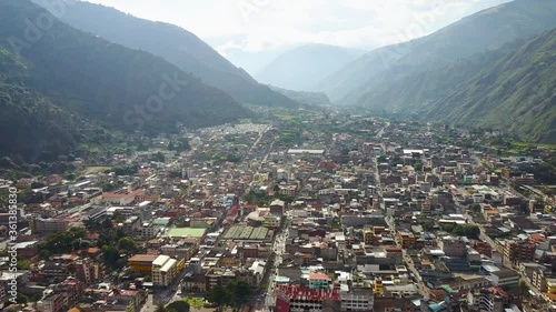 Wide Drone Aerial Long Shot Of Small Town With Short Buildings Settled On Valley Surrounded By A Green Lush Mountain Chain On A Beautiful Sunny Day In Ecuador