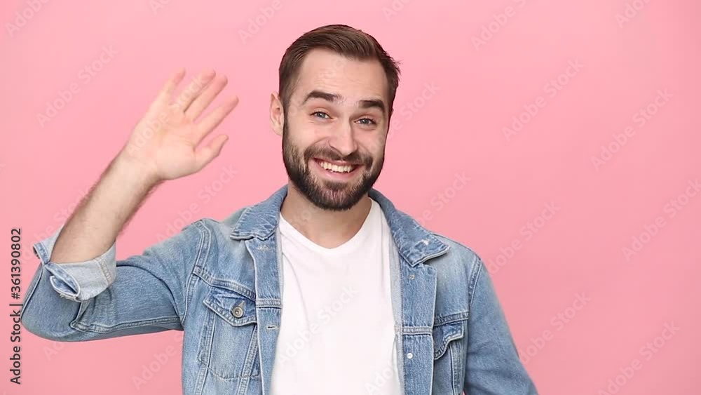Handsome young man guy 20s years old in denim jacket white t-shirt isolated on pastel pink background studio. People lifestyle concept. Looking camera waving and greeting with hand as notices someone Handsome young man guy 20s years old in denim jacket white t-shirt isolated on pastel pink background studio. People lifestyle concept. Looking camera waving and greeting with hand as notices someone