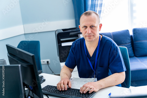 Man sitting at desk. Doctor in scrubs at office near computer. Office in hospital.