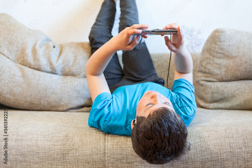 Lazy preteen boy playing game with his cellphone, child lying back on
