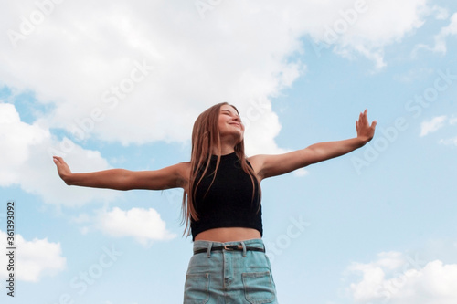 Portrait of a beautiful european woman breathing fresh air with raised arms with a cloudy blue sky in the background