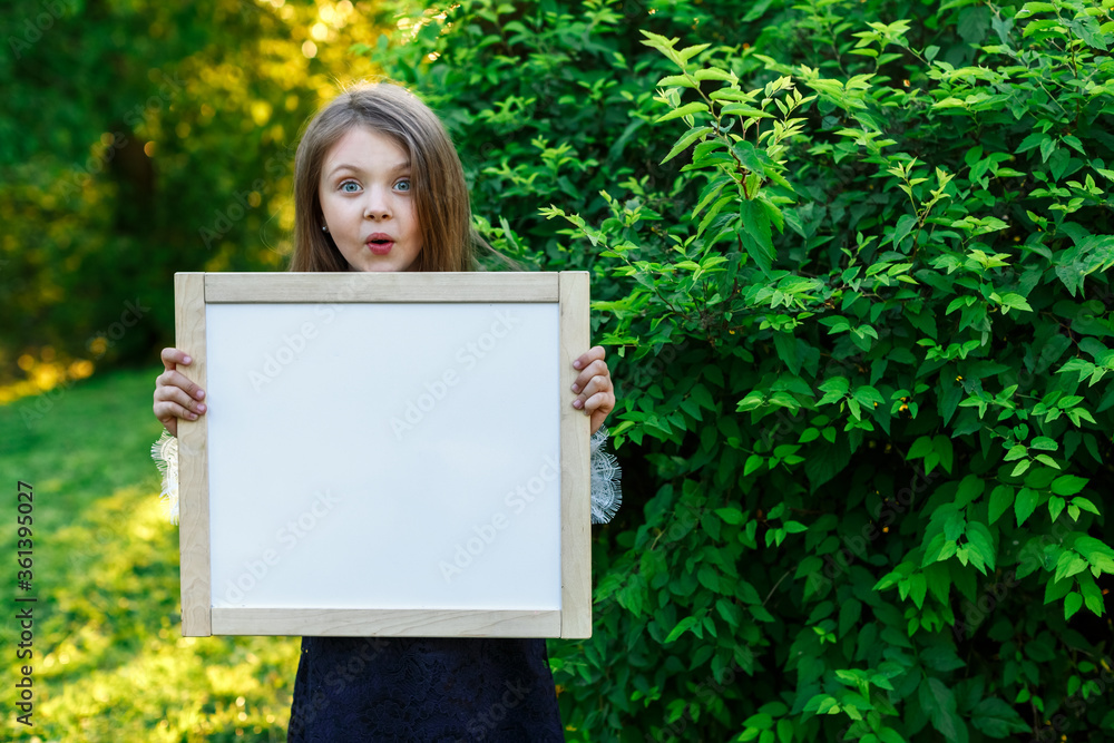 Surprised little girl in summer school uniform holding a white Board with space for text Surprised little girl in summer school uniform holding a white Board with space for text