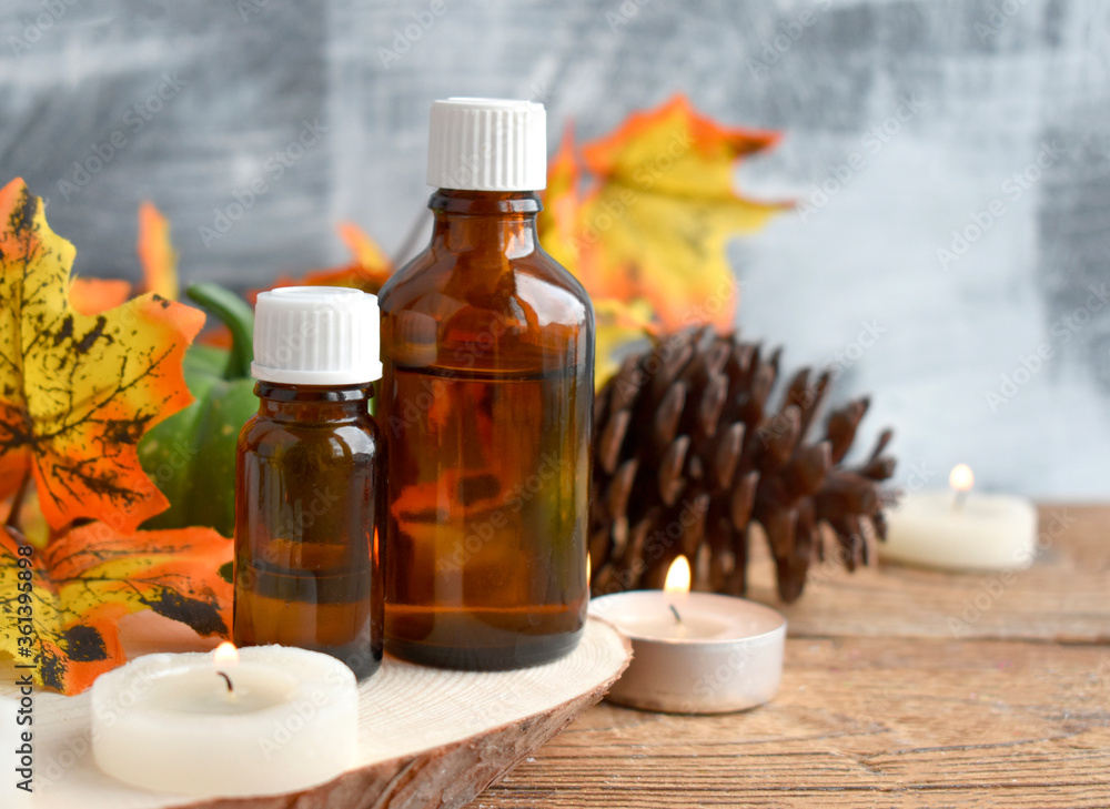 Close up autumn spa concept with essential oil bottle, dried leaves, burning candles on wooden background. Aromatherapy still life composition. Organic cosmetic.. Copy space. Close up autumn spa concept with essential oil bottle, dried leaves, burning candles on wooden background. Aromatherapy still life composition. Organic cosmetic.. Copy space.