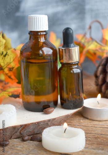 Close up autumn spa concept with essential oil bottle, burning candles on wooden background. Aromatherapy still life composition. Organic cosmetic..