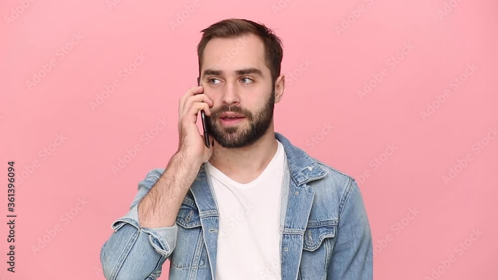 Angry bearded young man guy 20s years old in denim jacket white t-shirt talking screaming swearing to girlfriend using mobile phone isolated on pastel pink background studio. People lifestyle concept Angry bearded young man guy 20s years old in denim jacket white t-shirt talking screaming swearing to girlfriend using mobile phone isolated on pastel pink background studio. People lifestyle concept